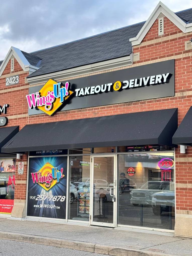 Wings Up storefront with illuminated logo sign, Takeout and Delivery letters, and window graphics